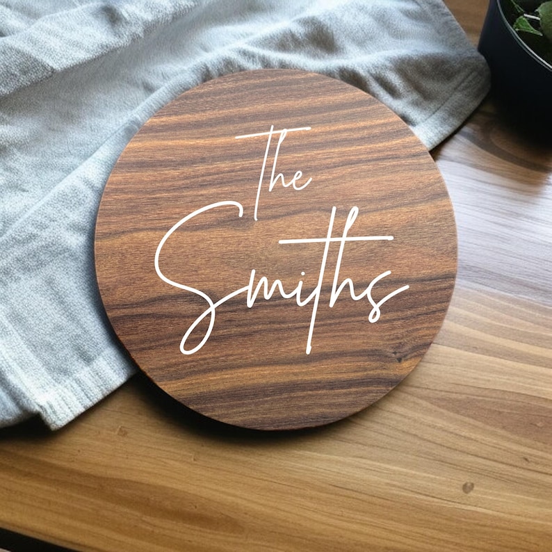 May include: A round wooden sign with the text "The Smiths" in white cursive lettering.