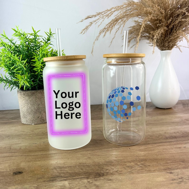 May include: Two glass tumblers with bamboo lids and straws. One tumbler is frosted and has the text "Your Logo Here" in black. The other tumbler is clear and has a blue geometric design.