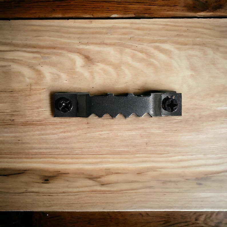 May include: A close-up of a wooden surface with a black metal hanging bracket attached to it. The bracket has two screws and a serrated edge.