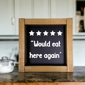 May include: A wooden sign with a black chalkboard insert. The chalkboard has five white stars and the text "Would eat here again".