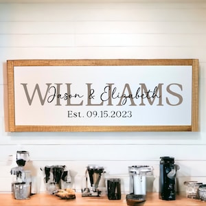 May include: A wooden sign with a brown frame and white background. The sign reads "WILLIAMS Jason & Elizabeth Est. 09.15.2023".