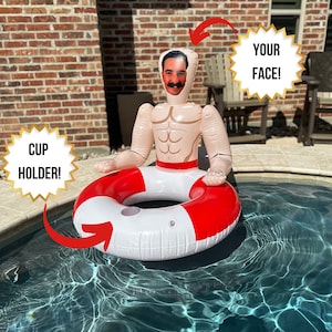 May include: Inflatable pool float shaped like a muscular man with a red and white life preserver. The float has a cutout for a face and the text "YOUR FACE!" is displayed. The text "CUP HOLDER!" is also displayed.