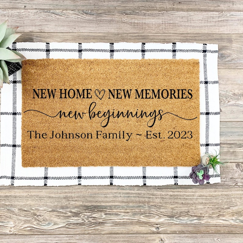 May include: A brown coir doormat with the text "NEW HOME &hearts; NEW MEMORIES new beginnings The Johnson Family ~ Est. 2023" printed in black.