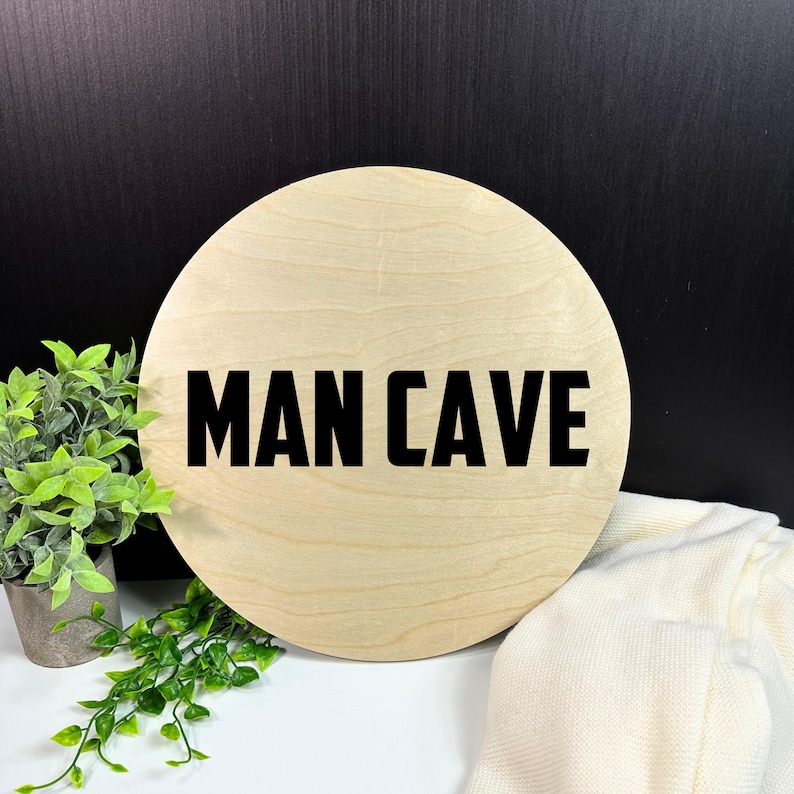 May include: A round wooden sign with the text "MAN CAVE" in black lettering.