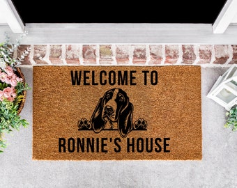 May include: A brown coir doormat with the text "WELCOME TO RONNIE'S HOUSE" and a black silhouette of a basset hound peeking over the top.