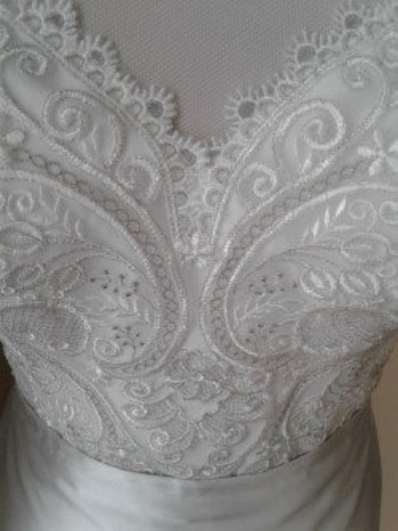 K&ouml;nnte beinhalten: Nahaufnahme eines wei&szlig;en Spitzenstoffs mit Paisley-Muster. Die Spitze ist zart und filigran, mit einem dezenten Glanz.