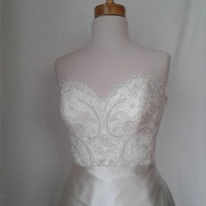 K&ouml;nnte beinhalten: Ein wei&szlig;es, tr&auml;gerloses Brautkleid mit einem Spitzenoberteil und einem Satinrock.