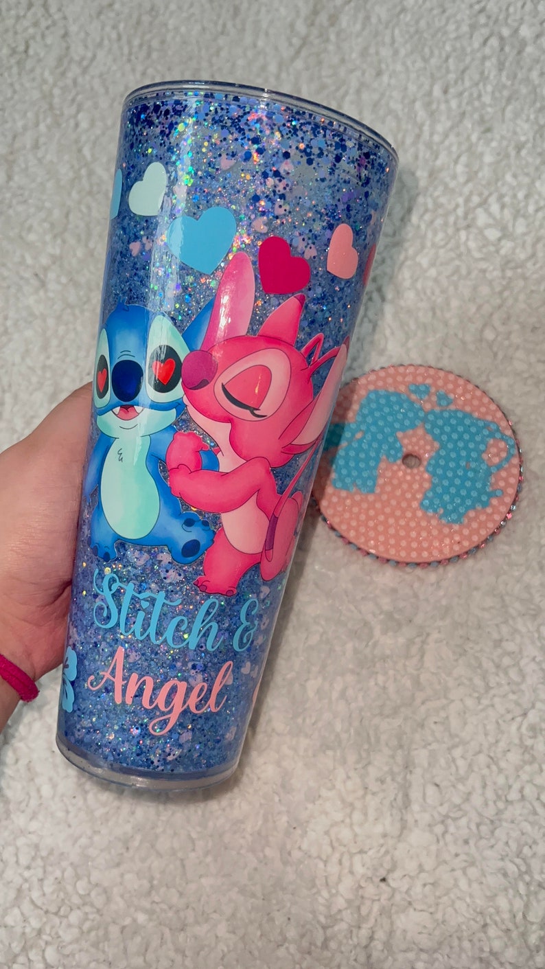 Może przedstawiać: Niebieski i r&oacute;żowy kubek z brokatem z obrazkiem Stitch i Angel z Lilo & Stitch. Kubek ma napis "Stitch & Angel".
