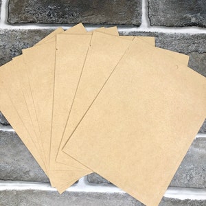 May include: A stack of blank, light brown paper cards with a small hole at the top. The cards are fanned out, revealing their rectangular shape. The background is a gray brick wall.