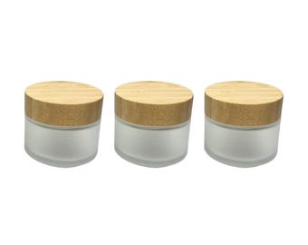 May include: Three frosted glass jars with natural bamboo lids. The jars are cylindrical with a wide base and a smooth, matte finish. The lids are round and made of light-colored bamboo.