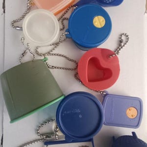 Op de afbeelding: Een verzameling kleurrijke, kleine plastic keukengadgets, waaronder bakjes, opscheplepels en zeven. De items zijn in tinten blauw, rood, groen en oranje en zijn bevestigd aan zilveren kogelkettingen. De items zijn ontworpen voor gebruik in de keuken.