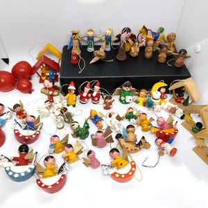 Puede incluir: Una gran colección de pequeños adornos de madera pintados a mano con diversas figuras, incluyendo ángeles, niños y animales en caballos balancín. Muchas piezas tienen lazos de hilo dorado para colgar y el conjunto incluye estructuras de madera.