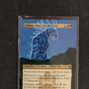 May include: A Magic: The Gathering trading card featuring a hand-painted blue elemental creature on a dark green landscape. The card text reads Animar, Soul of Elements, Legendary Creature - Elemental, with game rules and a 1/1 power and toughness.