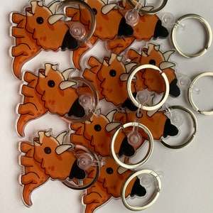 May include: A set of eight orange and black cartoon triceratops keychains with silver key rings.
