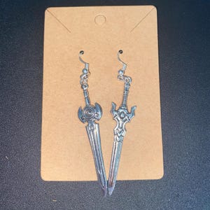May include: A pair of silver sword earrings. The swords have intricate details and are hanging from silver hooks.