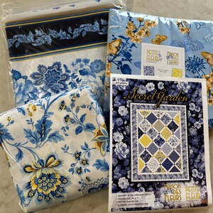 May include: A collection of floral fabric bundles and a quilt pattern titled "Secret Garden." The fabrics feature blue and white floral designs, with accents of yellow. The quilt pattern includes the text "Maison des Petites Fleurs."