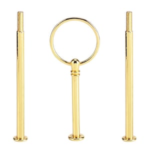 Könnte beinhalten: Goldfarbenes, dreiteiliges Tortenständer-Hardware-Set. Das Set enthält zwei Gewindestangen und ein Mittelteil mit Ringgriff. Die Teile bestehen aus glänzendem Metall und sind für den Zusammenbau eines mehrstöckigen Servierständer konzipiert.