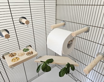 Pode incluir: Um conjunto de brinquedos de madeira para pássaros de gaiola, incluindo um prato de comida pendurado, um poleiro, um balanço e um suporte para rolo de papel higiênico. Os brinquedos são presos à gaiola com ventosas.