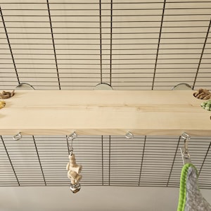 May include: A wooden shelf with four small bowls filled with different types of pet treats. The shelf is attached to a wire cage with hooks. There are two hanging toys attached to the shelf.