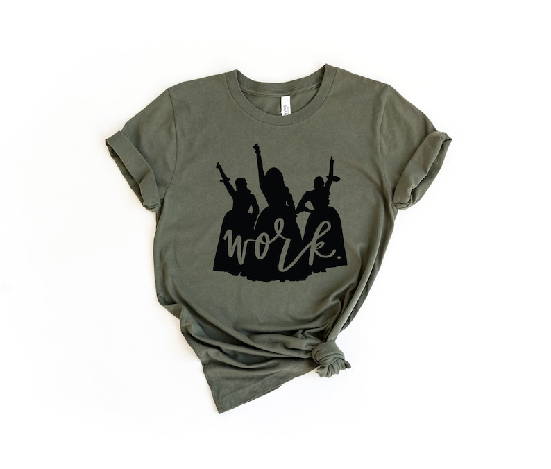 Peut inclure: Un t-shirt vert avec une silhouette noire de trois femmes en robes et le mot "work" &eacute;crit en cursive noire.