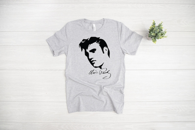 May include: A gray t-shirt with a black silhouette of Elvis Presley and his signature "Elvis Presley".