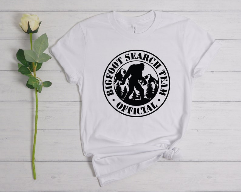 May include: White t-shirt with a black circle graphic that says "Bigfoot Search Team Official" with a silhouette of Bigfoot walking in the mountains.