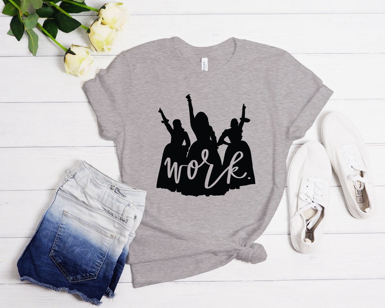 Peut inclure: Un t-shirt gris chin&eacute; avec une silhouette noire de trois femmes en robes et le texte "work" en &eacute;criture noire.