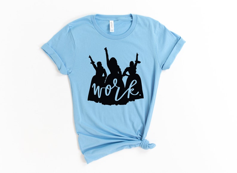 Peut inclure: T-shirt bleu clair avec une silhouette noire de trois femmes en robes et le mot "work" &eacute;crit en cursive noire.