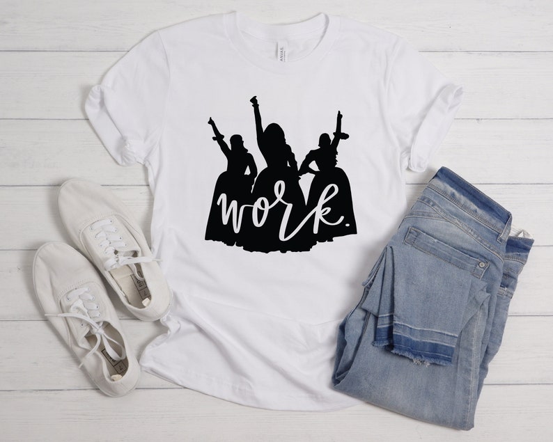 Peut inclure: T-shirt blanc avec une silhouette noire de trois femmes en robes et le mot "work" &eacute;crit en cursive en dessous.