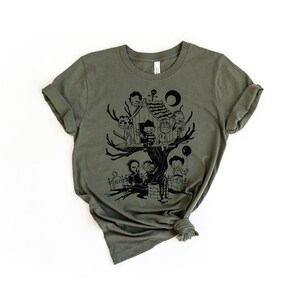 May include: A green t-shirt with a black graphic of a treehouse with spooky characters. The characters include a ghost, a vampire, a zombie, and a werewolf. The treehouse is surrounded by a graveyard.