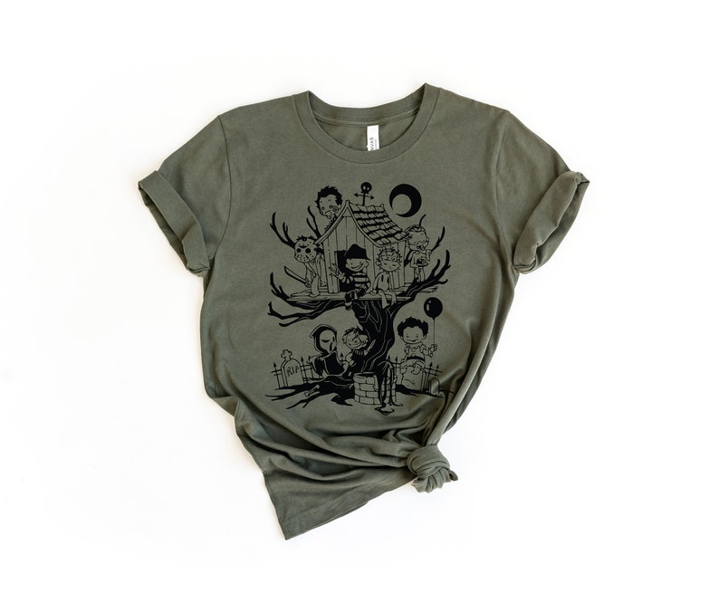 May include: A green t-shirt with a black graphic of a treehouse with spooky characters. The characters include a ghost, a vampire, a zombie, and a werewolf. The treehouse is surrounded by a graveyard.