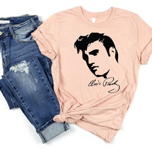 May include: A peach-colored t-shirt with a black silhouette of Elvis Presley's face and his signature.