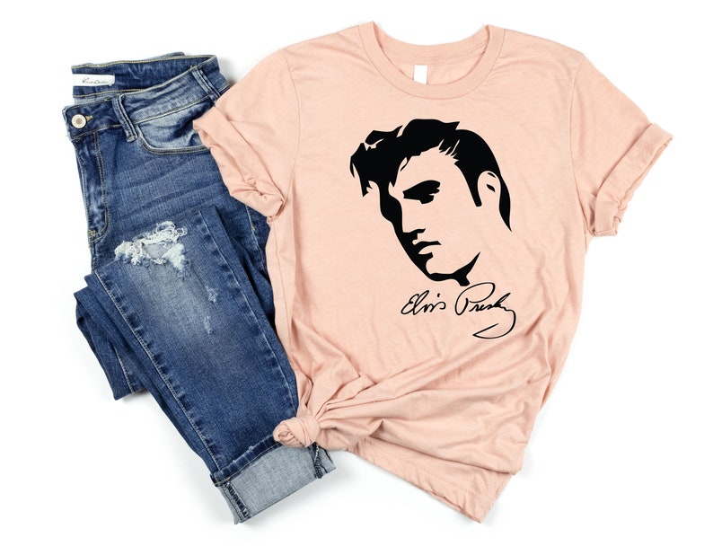 May include: A peach-colored t-shirt with a black silhouette of Elvis Presley's face and his signature.