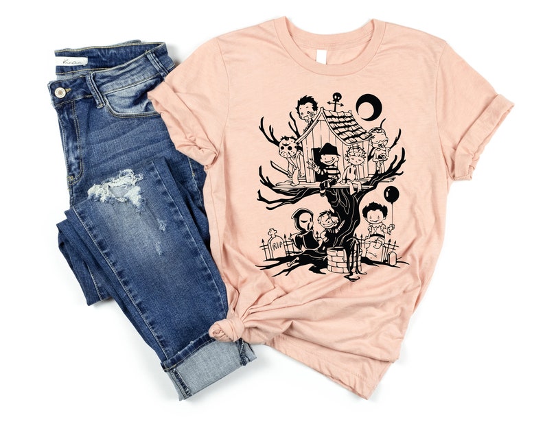May include: A peach-colored t-shirt with a black graphic of horror movie characters in a treehouse. The characters include Freddy Krueger, Jason Voorhees, Michael Myers, and others.