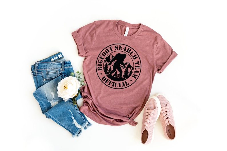 May include: A mauve t-shirt with a black circle graphic that says "Bigfoot Search Team Official" with a silhouette of Bigfoot walking in the woods.