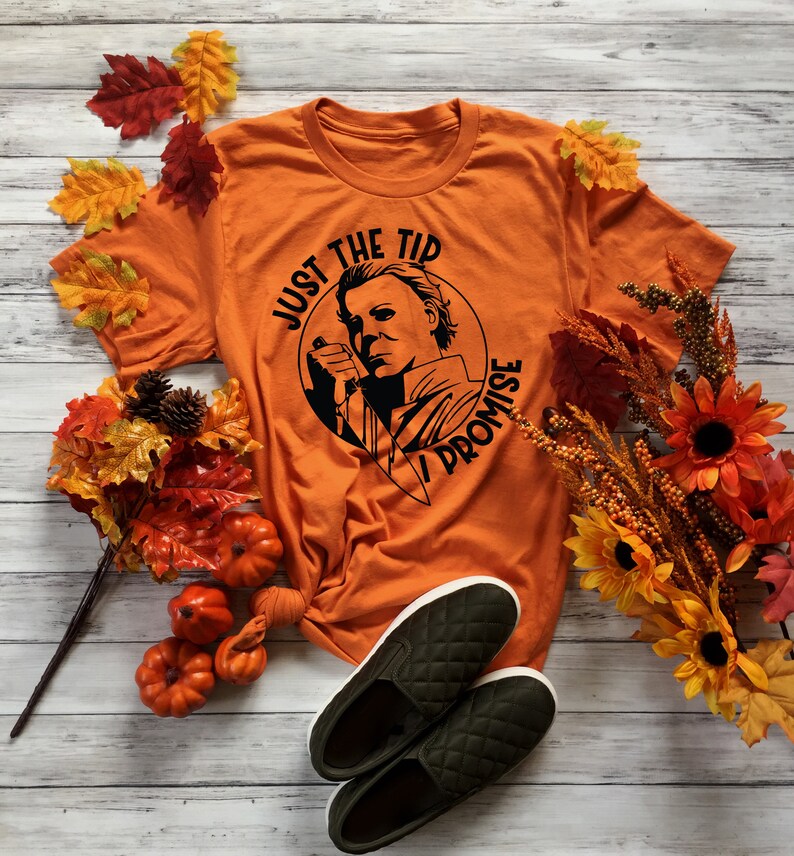 Pu&ograve; includere: Maglietta arancione con una grafica nera di Michael Myers del film Halloween. La grafica dice "Just the tip I promise".