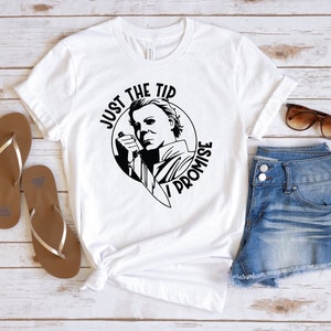 Pu&ograve; includere: Maglietta bianca con una grafica in bianco e nero di un personaggio che tiene un coltello. La grafica dice "Just the tip I promise".