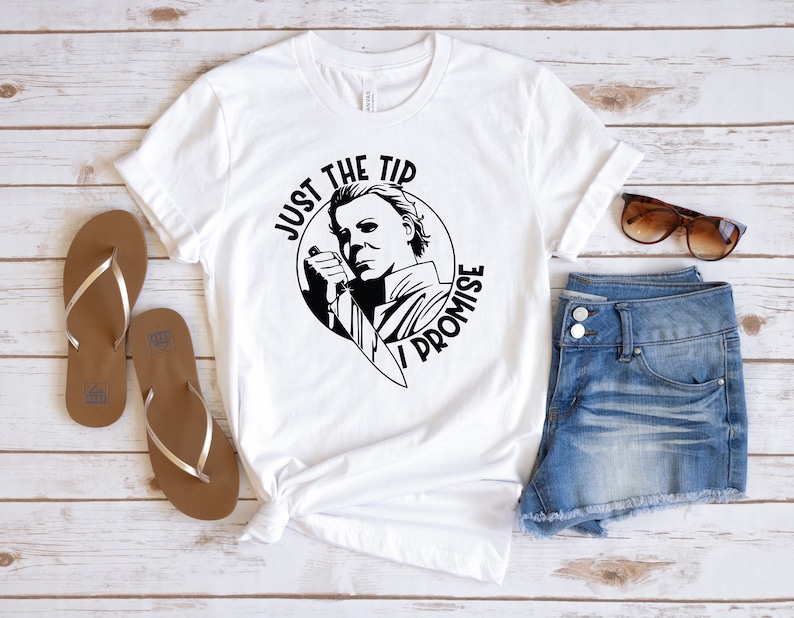 Pu&ograve; includere: Maglietta bianca con una grafica in bianco e nero di un personaggio che tiene un coltello. La grafica dice "Just the tip I promise".