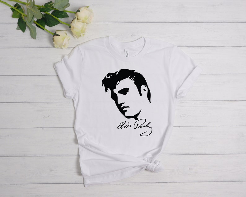 May include: White t-shirt with a black silhouette of Elvis Presley's face and his signature "Elvis Presley".