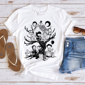 May include: A white t-shirt with a black and white illustration of horror movie characters in a treehouse. The characters include Freddy Krueger, Jason Voorhees, Michael Myers, and Leatherface. The text "RIP" is visible on a tombstone in the illustration.