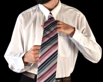 May include: A striped tie with a pattern of pink, gray, black, and blue is being adjusted. The tie is worn with a white dress shirt and black pants. The background is black.