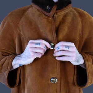 May include: A brown suede jacket with a shearling collar and a button closure. The jacket has a relaxed fit and is perfect for layering.