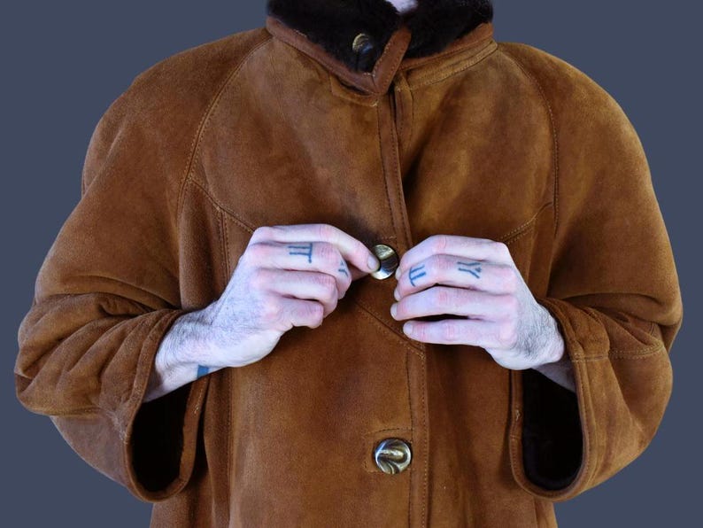 May include: A brown suede jacket with a shearling collar and a button closure. The jacket has a relaxed fit and is perfect for layering.