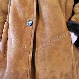 May include: A brown suede coat with a button closure and a black fur trim on the sleeves.