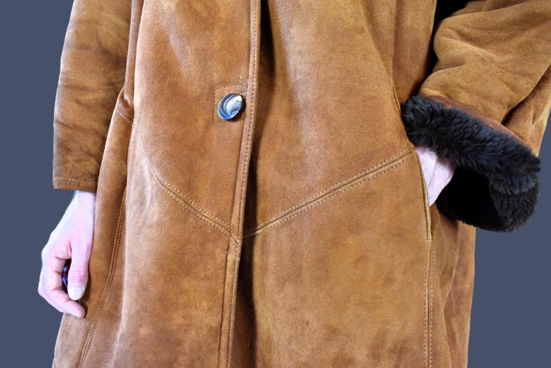 May include: A brown suede coat with a button closure and a black fur trim on the sleeves.