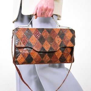 May include: A vintage handbag with a geometric pattern of brown, black, and tan diamonds. The bag has a flap closure, a top handle, and a long shoulder strap. The handle and frame are silver-toned.