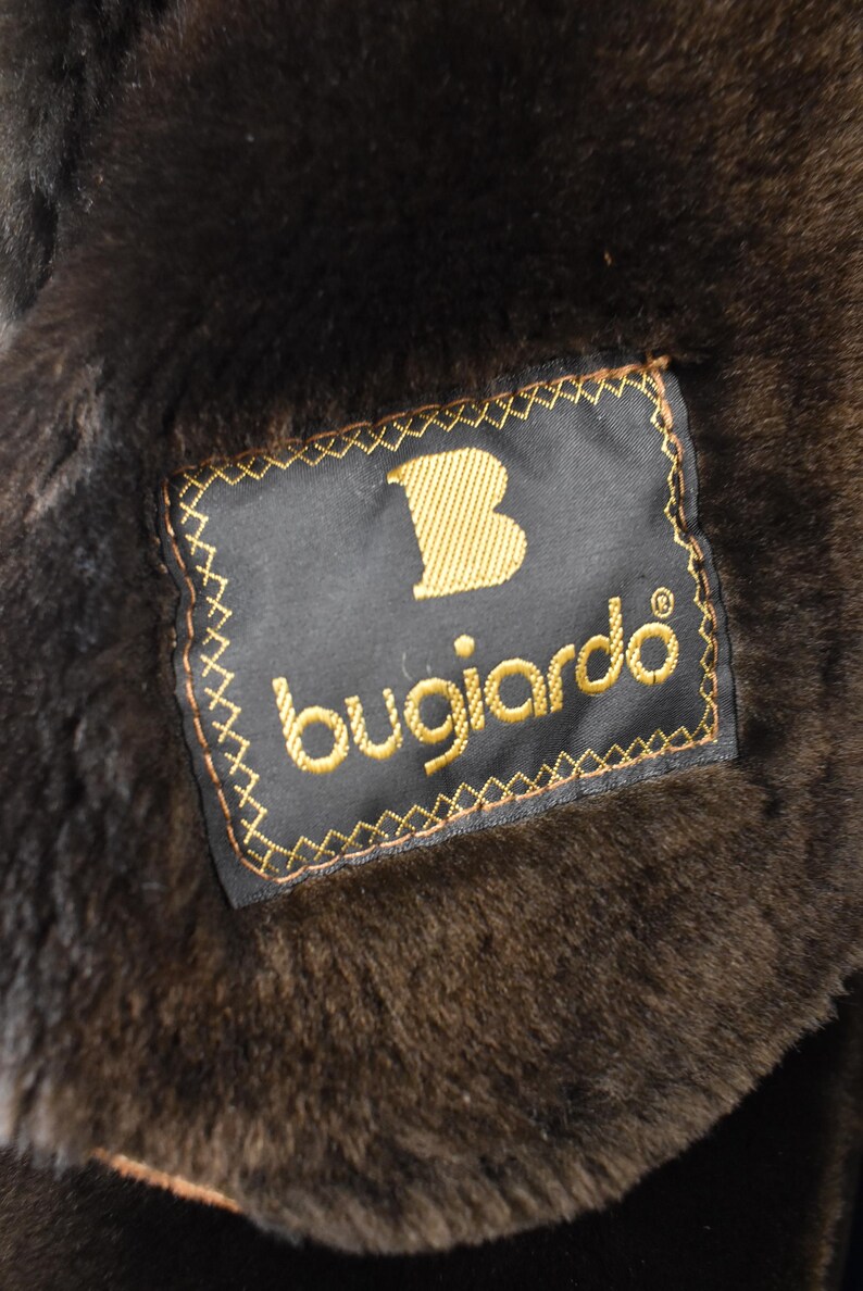 May include: A black fur coat with a brown leather label that says "Bugiarde" with a gold "B" in the upper left corner.