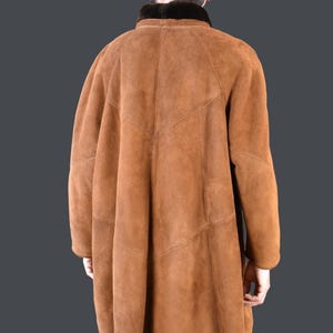 May include: A brown suede shearling coat with a black fur collar. The coat has a long, loose fit and a straight hemline.