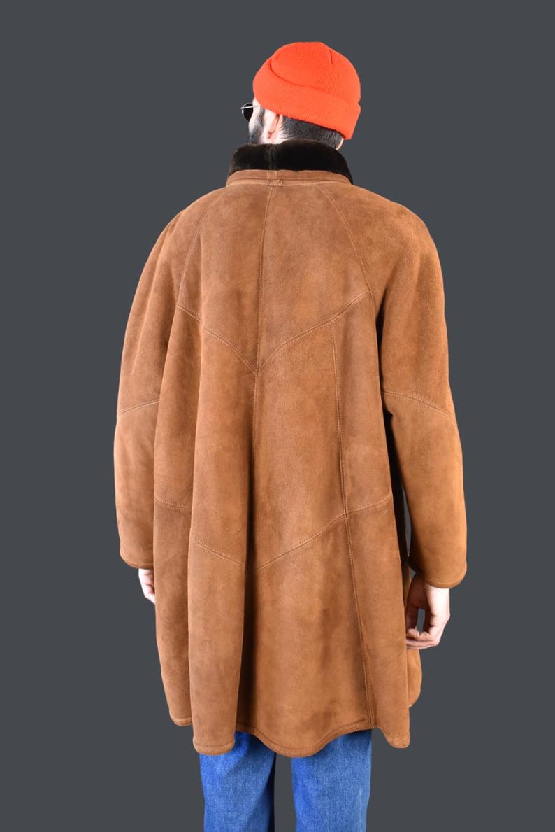 May include: A brown suede shearling coat with a black fur collar. The coat has a long, loose fit and a straight hemline.