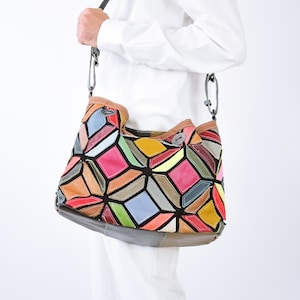 Könnte beinhalten: Eine Umhängetasche mit einem mehrfarbigen, geometrischen Patchwork-Design aus Lederstücken in Rot-, Gelb-, Blau-, Grün- und Orangetönen, die durch schwarze Linien getrennt sind. Die Tasche hat einen dunklen Riemen und metallische Befestigungselemente.